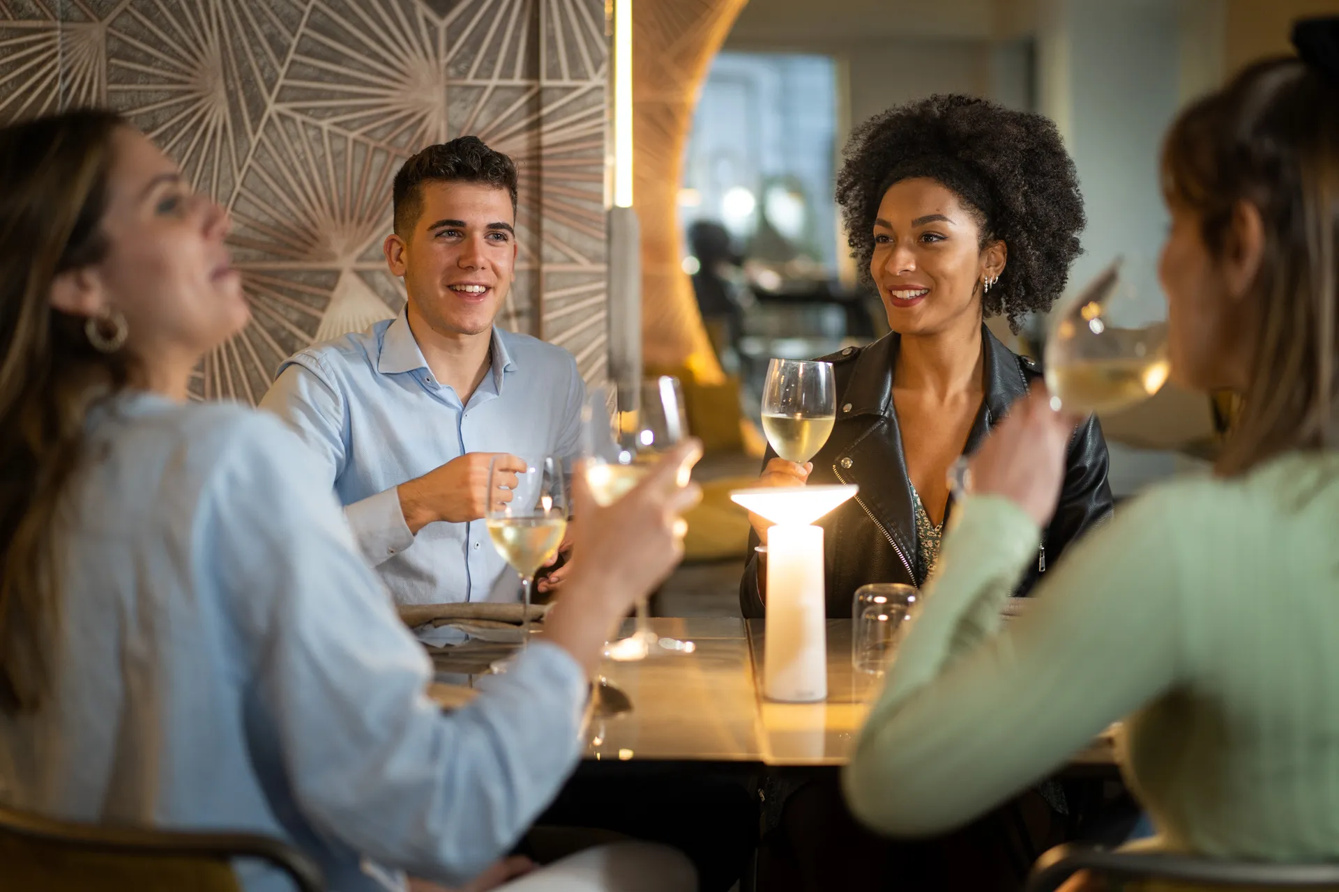 Four friends smiling over wine glasses at a candlelit restaurant table on a weeknight evening.