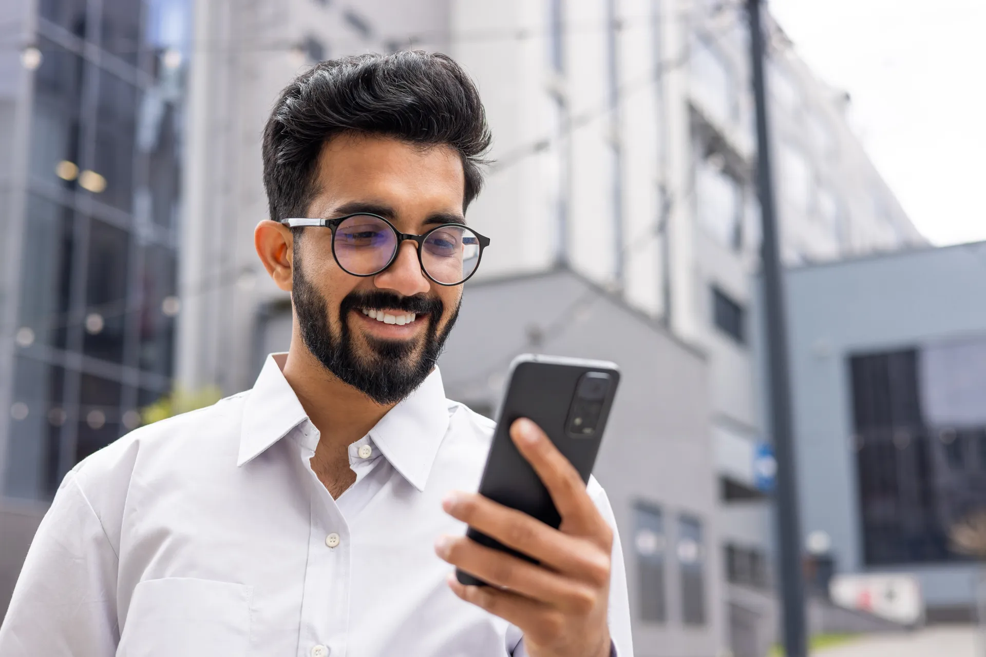 An agent smiling as he checks a form update on his phone outside the office.