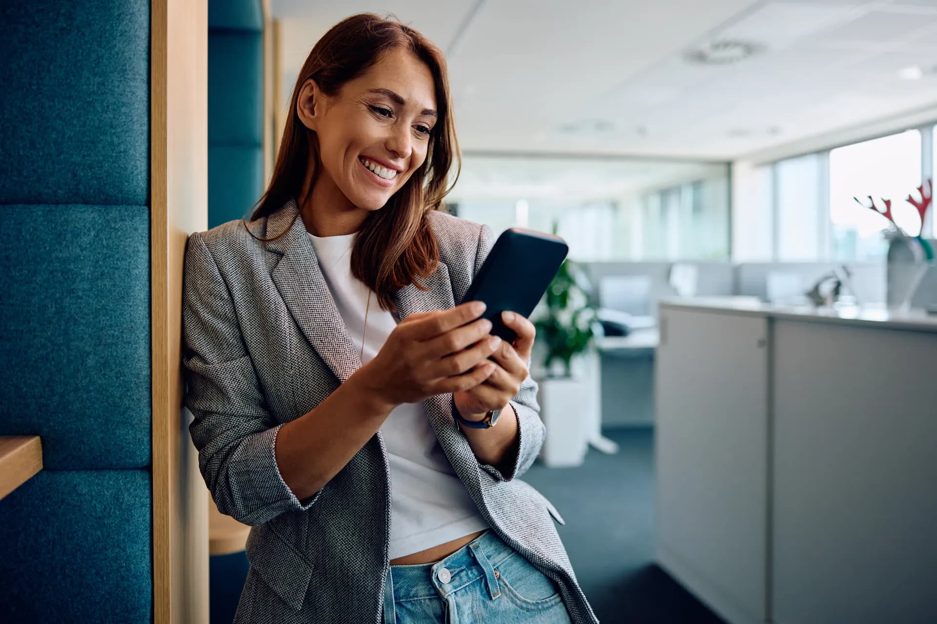 A real estate agent smiling as she checks a pipeline update on her phone in a bright office.