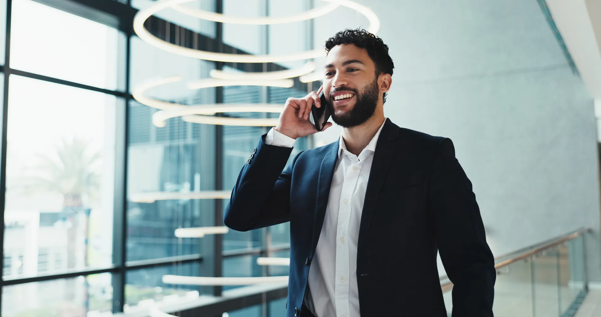 A broker on a call in a bright, glass-walled office lobby.
