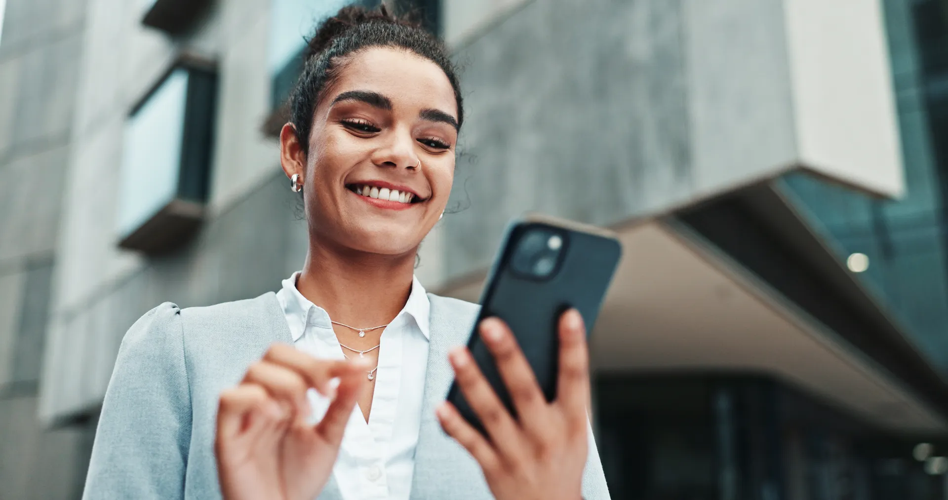 An agent smiling as she reads a new lead notification on her phone outside her office.